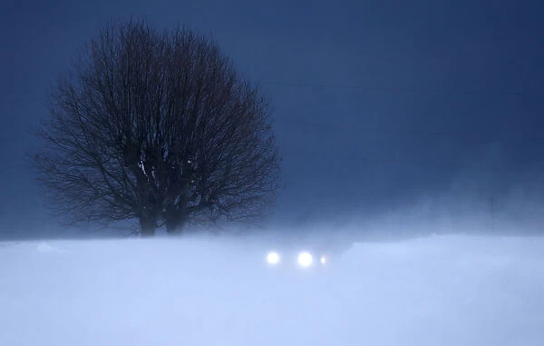 The lights of a car are seen through a gust of wind on a secondary road in Lussy near