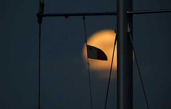 A Maltese flag flies from a yachts mast as a supermoon full moon rises in Pieta