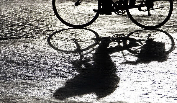 A man casts a shadow as he rides his bicycle