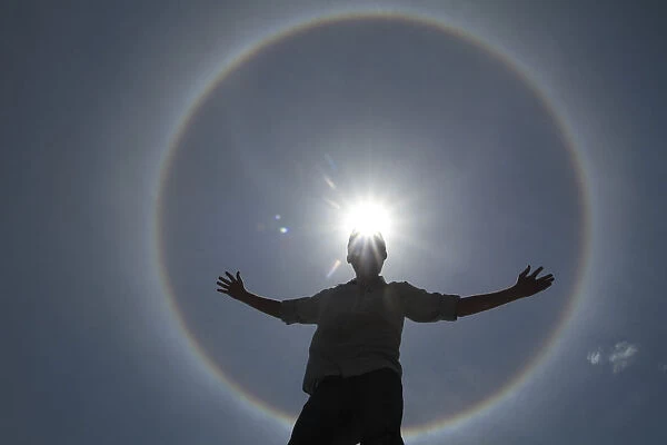 A man poses for photos as solar halo is seen in the sky of Brasilia