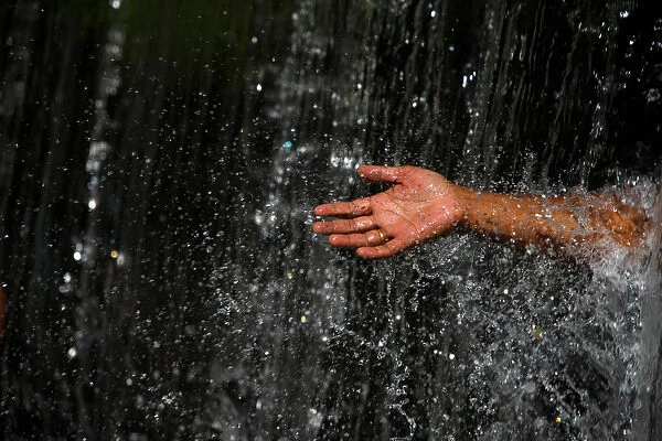 A man takes out his hand throughout the waterfall at Muhan Pokhari in Bhaktapur