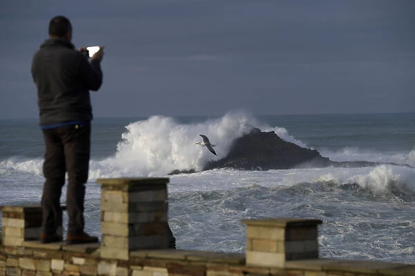 A man takes pictures of waves as they crash against a lighthouse in the port town of