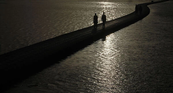 Men are silhouetted against the setting sun as they walk by the sea in Karachi