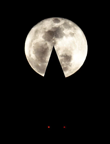 The full moon rises behind the Washington Monument in Washington