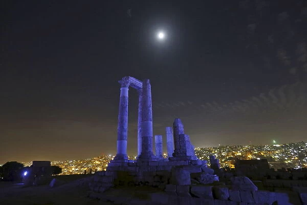 The moon is seen over the Roman pillars of the Temple of Hercules as it is lit up in blue
