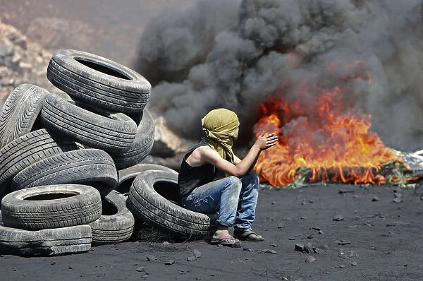 A Palestinian boy sits next to burning tyres during cashes with Israeli soldiers