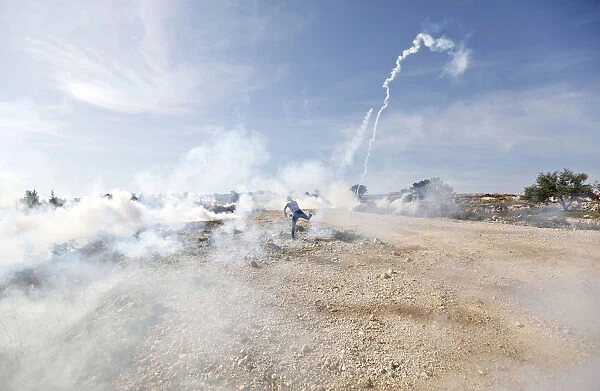 A Palestinian protester throws back a tear gas canister fired by Israeli troops during