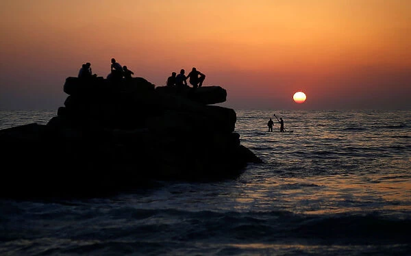 Palestinians ride a boat in the Mediterranean Sea as others enjoy the beach during