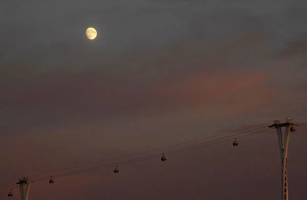 Passengers cross the River Thames in cable cars with the moon seen behind at dusk