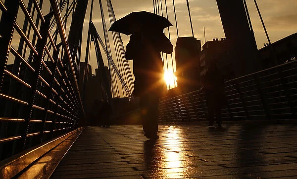 A pedestrian carries an umbrella as he walks over one of the Golden Jubilee Bridges in