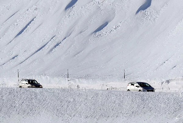 People drive their cars slowly on a snow-covered road in Saint-Pancrace as winter weather