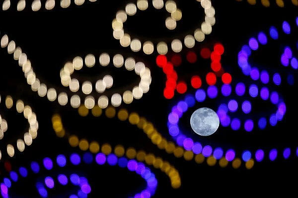 The rising full moon is seen behind Christmas lights in Valletta