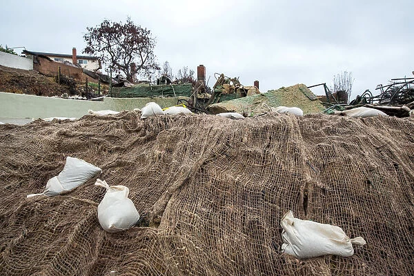 Sandbags and webbing are seen on a small hill in front of a house burned to the ground in