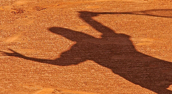 A shadow of a tennis player falls on the red clay of the central court at the Estoril