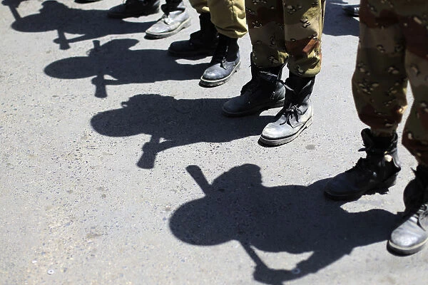 Shadows of army soldiers holding batons are cast on the ground as they stand in line to