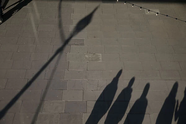 The shadows of pedestrians are cast on the pavement as they walk along the South Bank in