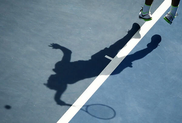 A tennis player casts a shadow as he serves