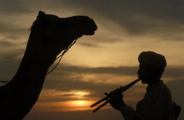 Villager plays flute as he is silhouetted against the setting sun over the Thar Desert