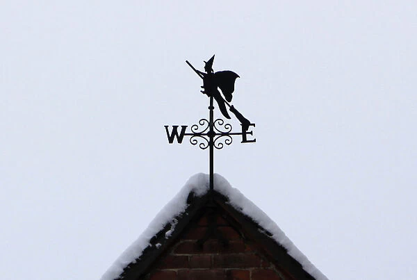 A weathervane in the shape of a witch on a broomstick is seen on the snow-covered roof of