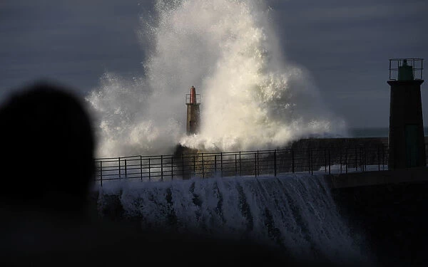 A woman looks at waves as they crash against a lighthouse in the port town of Viavelez