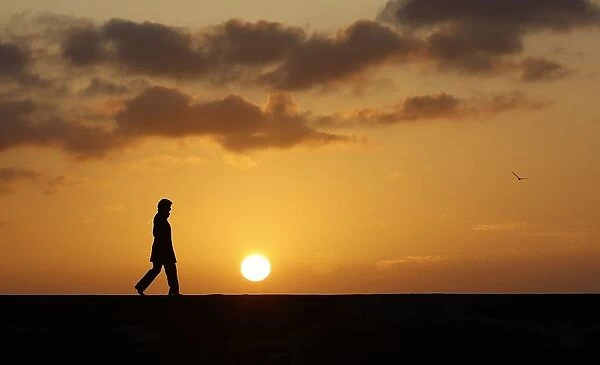 A woman walks along a breakwater at sunset in Sennen Cove, near Lands End, at the