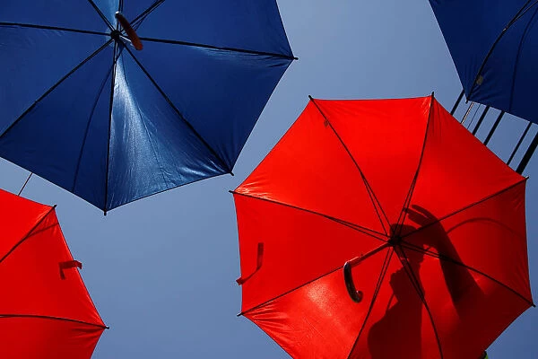 A worker arranges coloured umbrellas hanging over a street in preparation for a music
