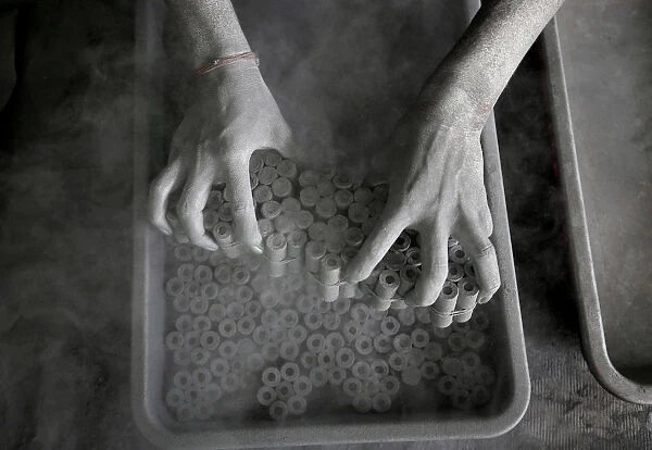 A worker removes paper rolls after filling them with gunpowder mixture to make