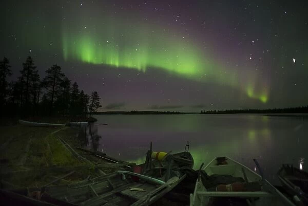 Aurora Borealis and stars over lake with beached canoes at night, Muonio, Lapland, Finland, September