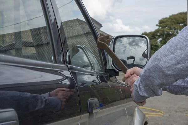 Man trying to break pick-up window with metal bar in farmyard, Lancashire, England, August