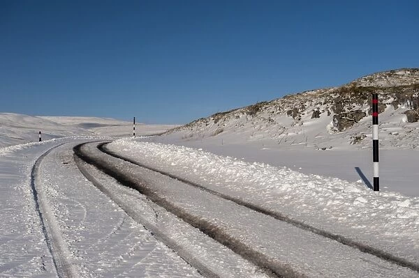 Snow covered road on moorland, with poles indicating snow depth levels, Yorkshire Dales N. P