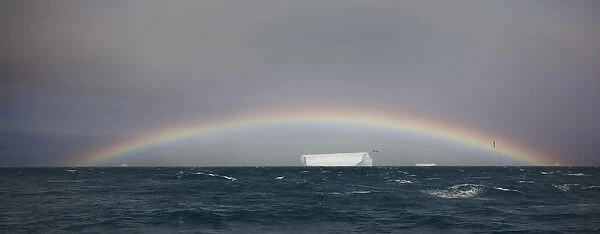 Antarctica, South Georgia, South Atlantic Ocean. A tabular iceberg floats under a low rainbow
