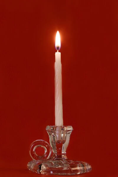 Burning candle in a glass candle holder on red background