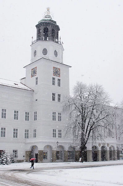 Europe, Austria, Salzburg. Person in snowstorm with red umbrella walking past white building