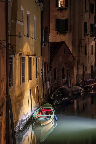 Europe, Italy, Venice. Wooden boat and reflections on still canal at night
