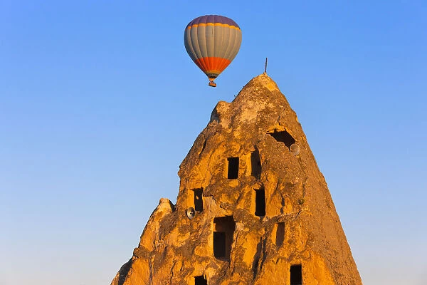 Hot air balloon over houses carved into rock formations, Uchisar, Cappadocia, Turkey