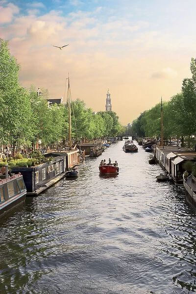Netherlands, Amsterdam, Boats cruise along a canal with the Zuiderkerk bell-tower in the background