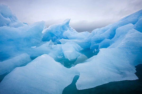 Norway, Svalbard, Spitsbergen Island, Summer snow storm above deep blue glacial iceberg