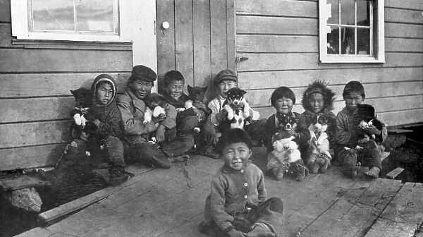 ALASKA: ESKIMO CHILDREN. A group of Eskimo children, some holding puppies, sitting