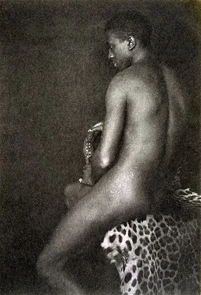DAY: NUDE, c1897. Portrait of a nude man sitting on a leopard skin