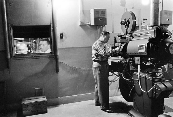 MOVIE PROJECTOR, 1958. A man working with a projector at an American movie theater