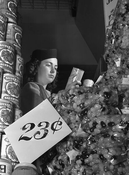 SHOPPING, 1942. A woman inspecting the labels on canned goods in a supermarket