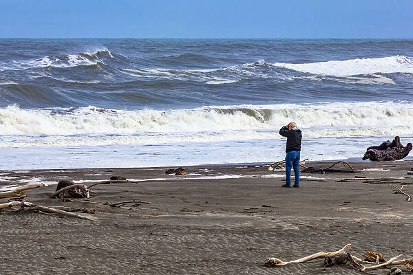 A photographer photographing the waves on the beach at Hokitika in West Coast, New Zealand