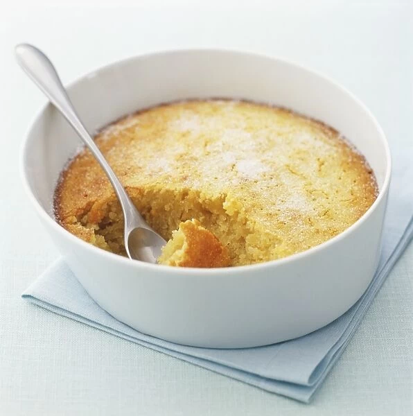 Baked almond pudding in a pie dish, spoon embedded