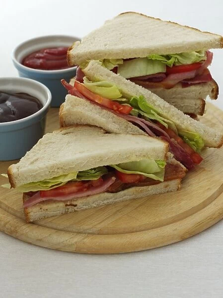 BLT sandwiches served with bowls of home-made brown sauce and tomato sauce, on chopping board, close-up