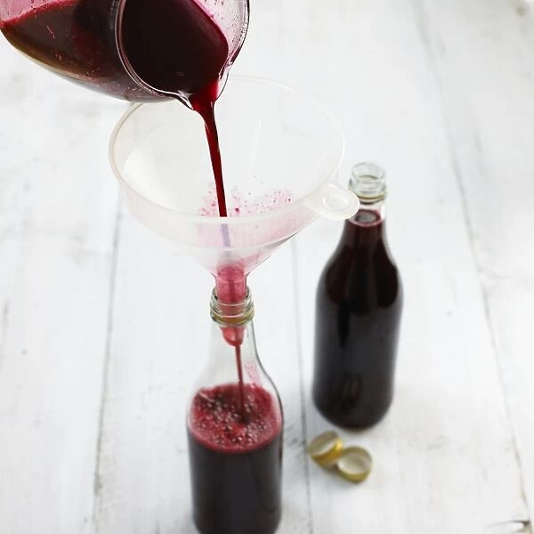 Bottling blackberry cordial, pouring through funnel, close-up