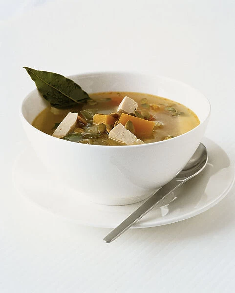 Bowl of chunky vegetable soup with pumpkin, pumpkin seeds, tofu, garnished with bay leaf