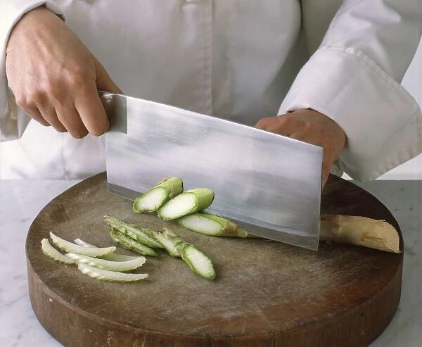 Chefs hands chopping asparagus with cleaver, chopped fennel nearby, close-up