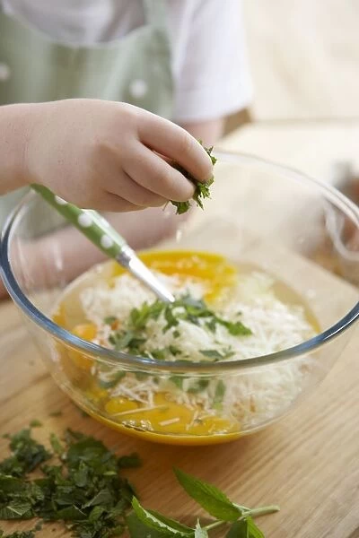 Child adding mint and pecorino to egg mixture in bowl (making frittata omelette)