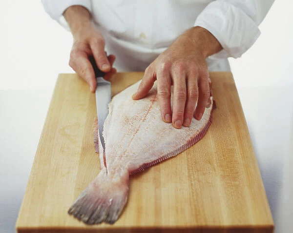 Flat fish being filleted with a knife on chopping board, high angle view