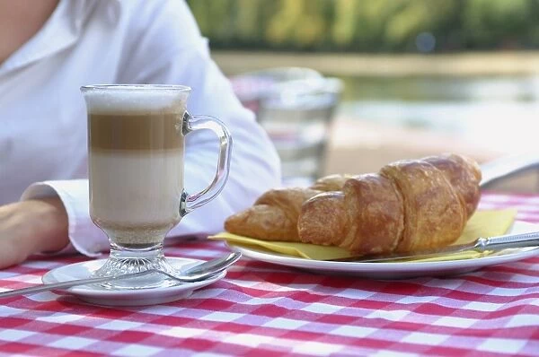 France, woman with cafe latte and croissant on table